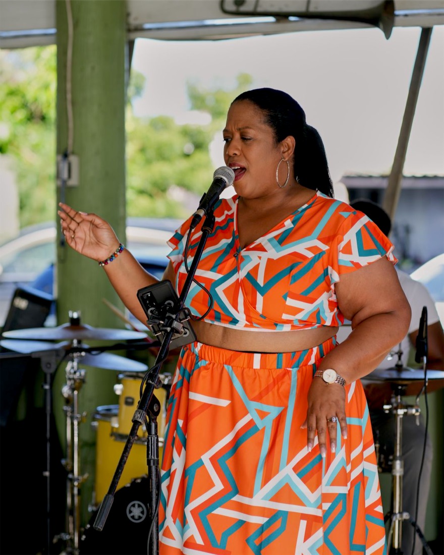 Queen B singing outdoors in an orange print