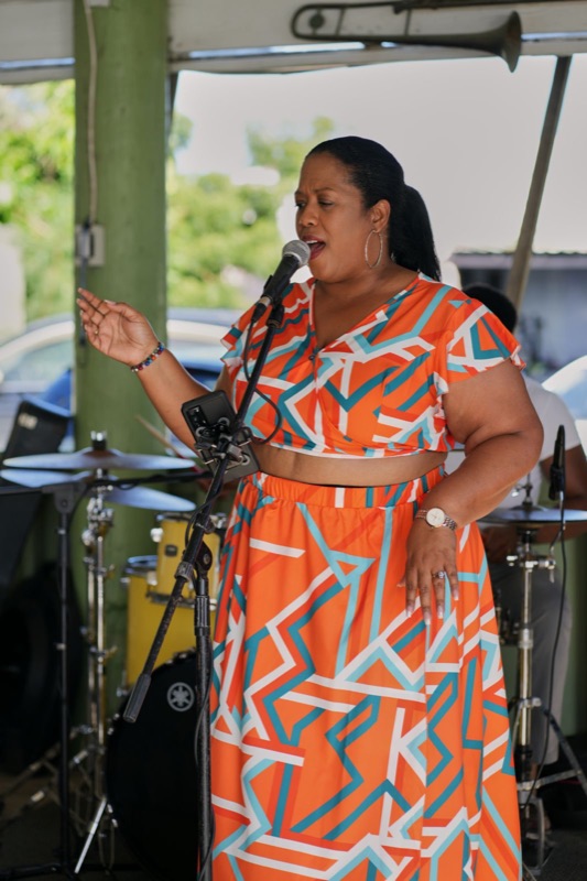 Queen B in an orange geometric dress singing outdoors